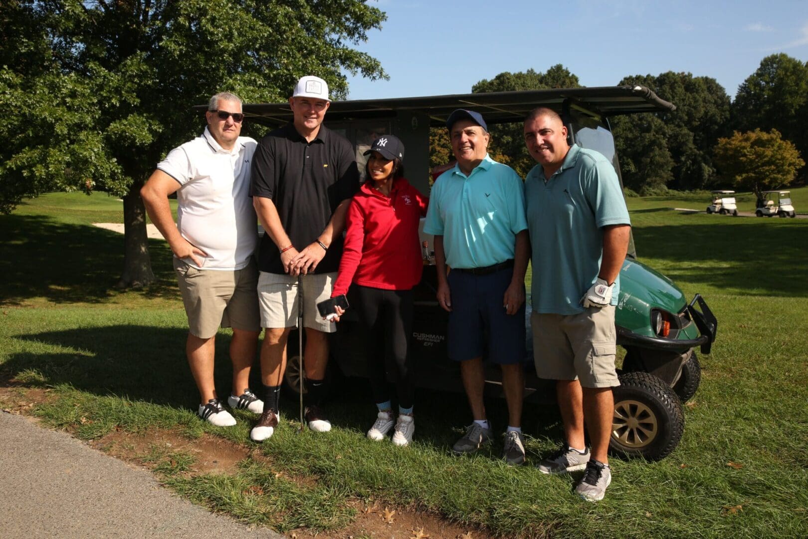 Five people posing by a golf cart.