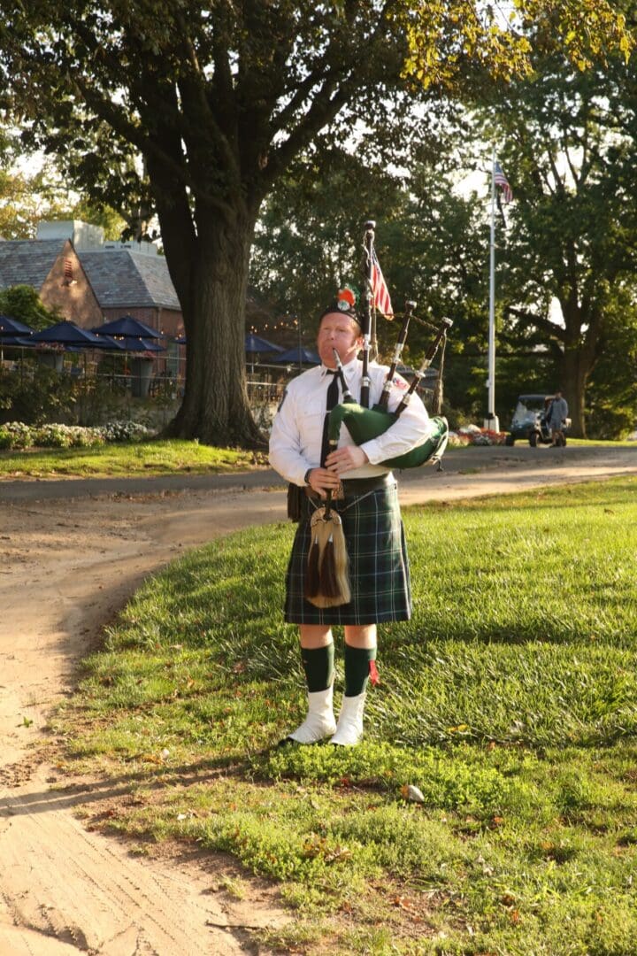 Man in kilt plays bagpipes outside.