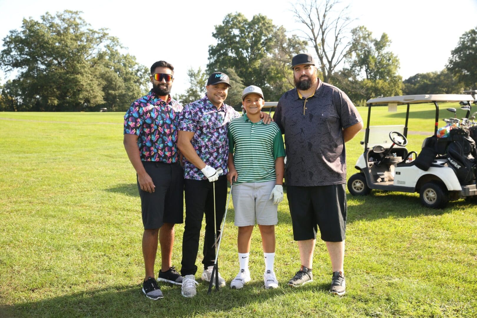 Four men on a golf course with a golf cart.